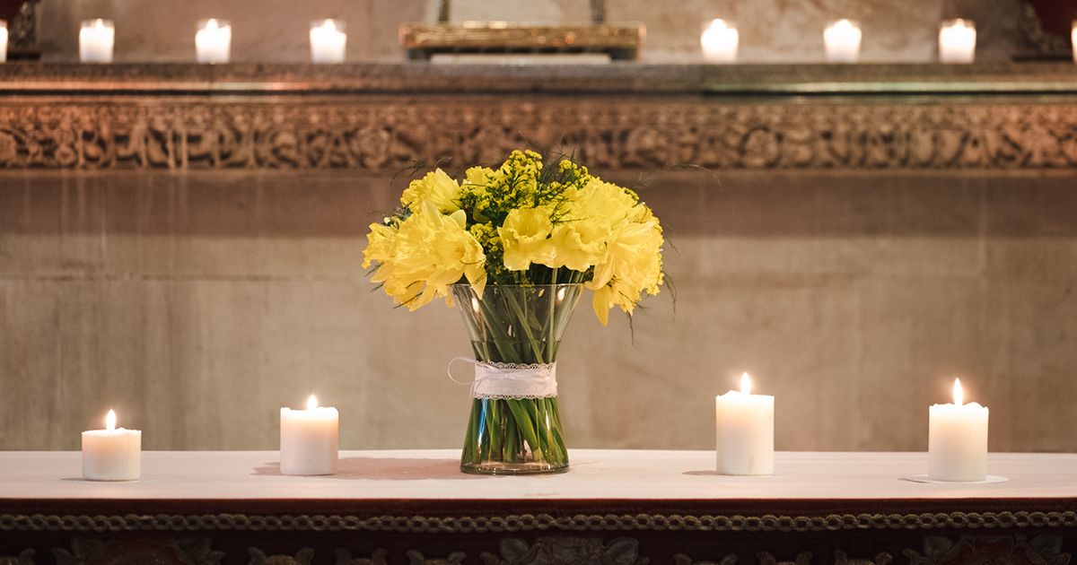 Bouquet of yellow daffodils in a clear vase, surrounded by lit candles
